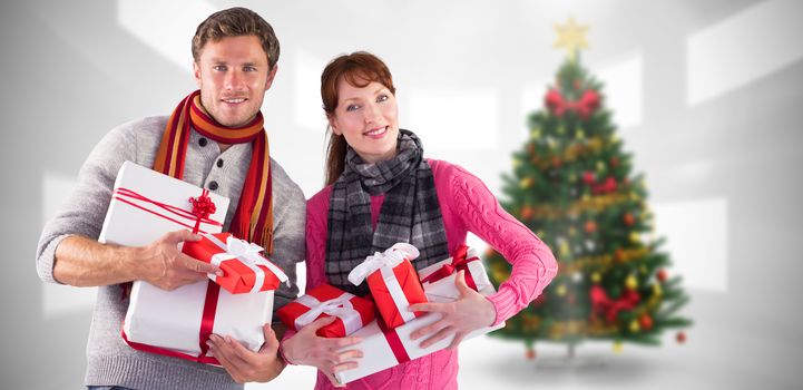 Couple holding lots of presents against home with christmas tree