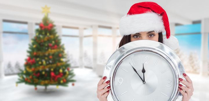 Festive brunette holding a clock against home with christmas tree