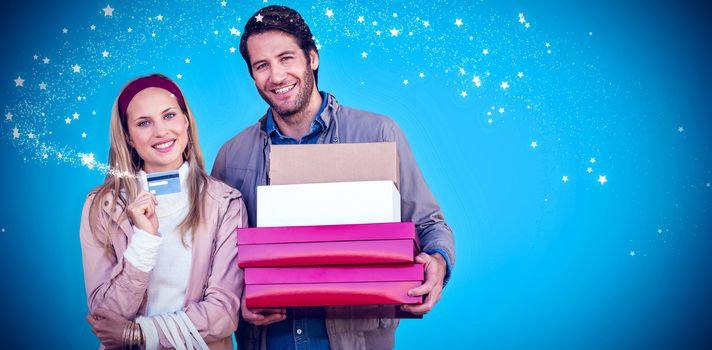 Smiling couple showing credit card and carrying boxes against blue background with vignette