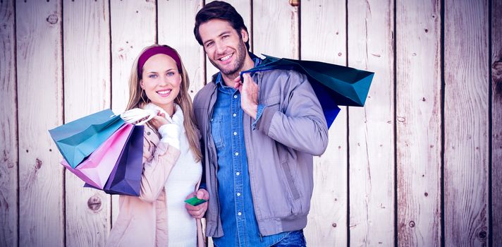 Smiling couple with shopping bags in front of window against wooden planks