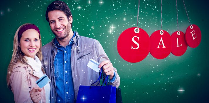 Smiling couple with shopping bags showing credit card against green