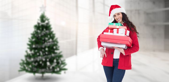 Festive brunette in santa hat and red coat holding pile of gifts against home with christmas tree