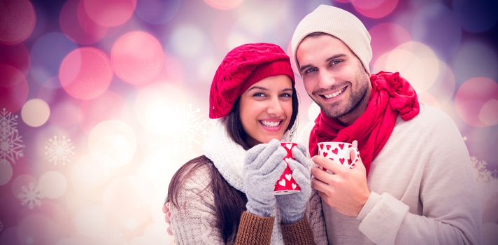 Winter couple holding mugs against glowing christmas background