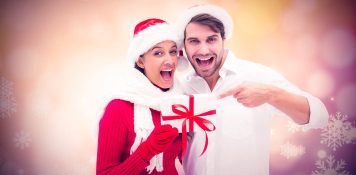 Festive young couple holding gift against glowing christmas background