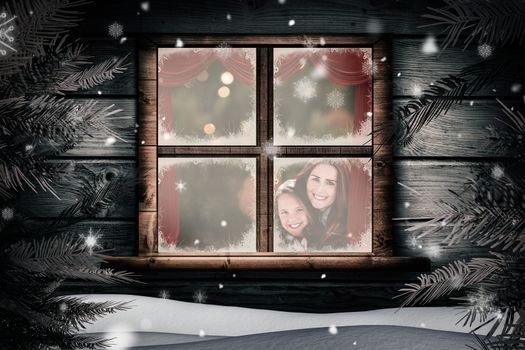 Mother and daughter under blanket against christmas home seen through frosty window