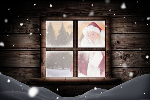 Santa asking for quiet to camera against fir tree forest in snowy landscape