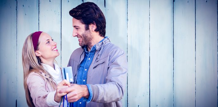 Smiling couple showing credit card and shopping bags against wooden planks