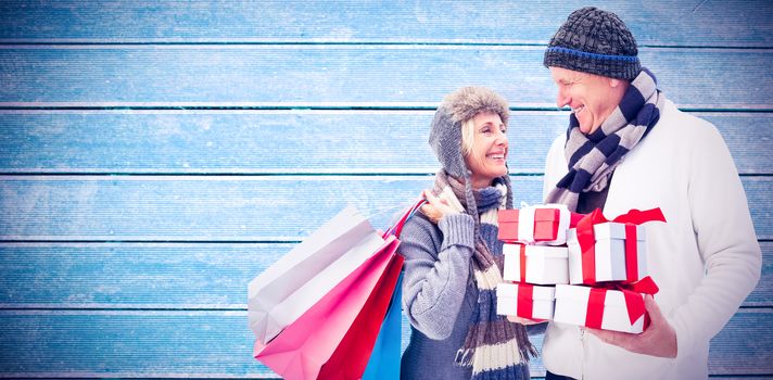 Festive mature couple holding christmas gifts against wooden planks