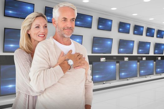 Cheerful wife embracing husband against televisions for sale
