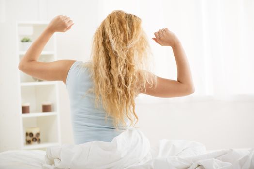Cute young woman awakening in the morning. She is stretching in the bed. Rear view