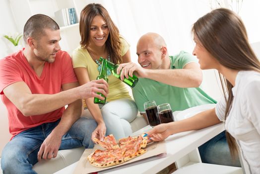 Friends enjoying eating pizza and drink a beer together at home party.