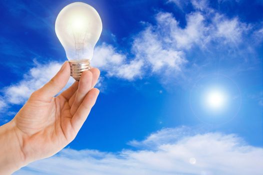 Ecological energy. Hand holds a light bulb against blue sky.