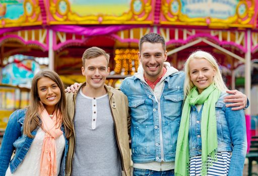 leisure, amusement park and friendship concept - group of smiling friends with carousel on the back