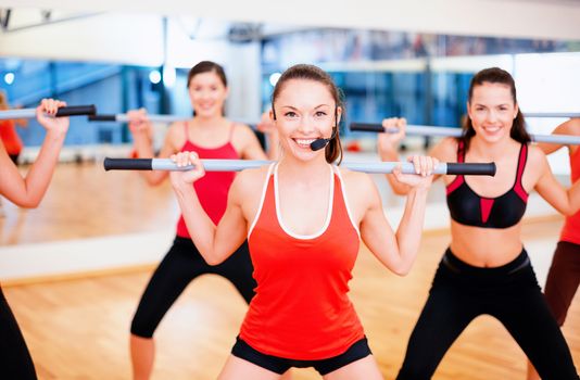 fitness, sport, training, gym and lifestyle concept - smiling trainer in front of the group of people working out with barbells in the gym