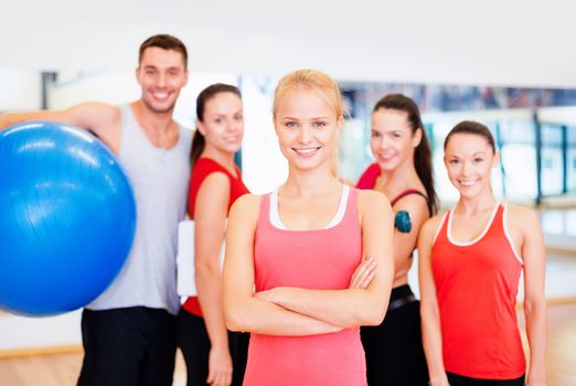 fitness, sport, training, gym and lifestyle concept - smiling woman standing in front of the group of people in gym