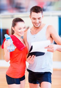 fitness, sport, training, gym and lifestyle concept - smiling male trainer with clipboard and woman with water bottle in the gym