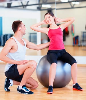 fitness, sport, training, gym and lifestyle concept - male trainer with woman doing crunches on the ball