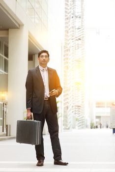 Portrait of fullbody Asian Indian business man standing outside modern office building block, beautiful golden sunlight at background.