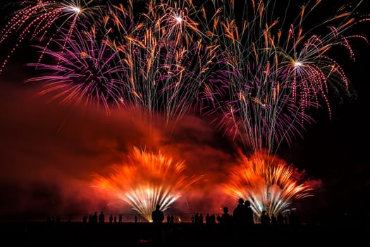 Colorful fireworks of various colors over night sky with spectators