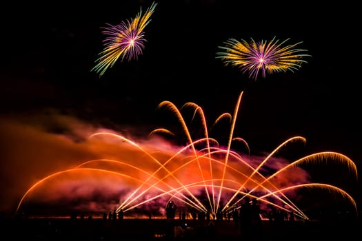 Colorful fireworks of various colors over night sky with spectators