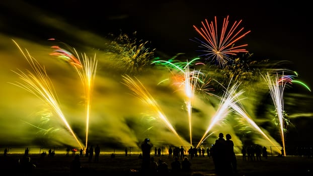 Colorful fireworks of various colors over night sky with spectators