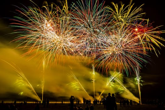 Colorful fireworks of various colors over night sky with spectators