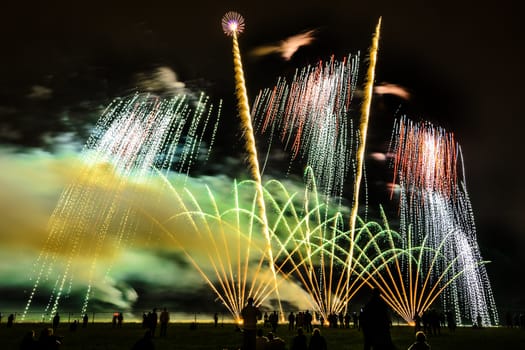 Colorful fireworks of various colors over night sky with spectators