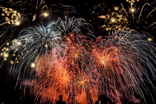 Colorful fireworks of various colors over night sky with spectators