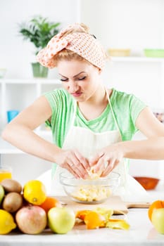 Beautiful young woman preparing orange for fruit salad in a kitchen. 