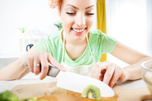 Beautiful young woman cutting kiwi in a kitchen. 