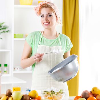 Beautiful young woman preparing fruit salad with Whipped Cream in a kitchen. Looking at camera.