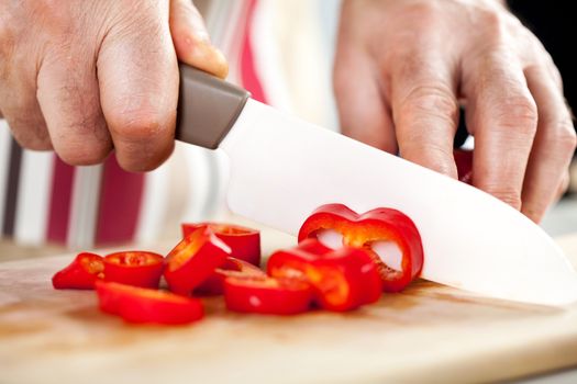 Senior Male Hands Cutting red peppers on the kitchen board.