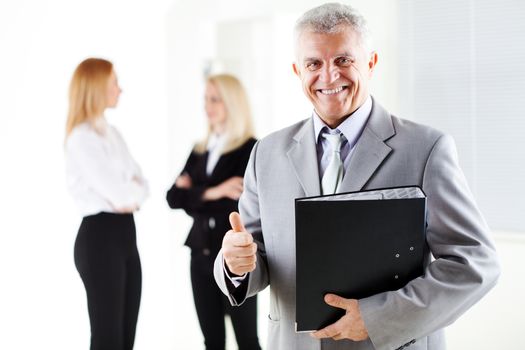 Happy senior businessman with folder in the office, showing thumbs. Looking at camera. Selective Focus. 