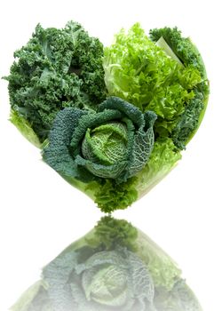 Heart shape green vegetables including cabbage and kale over a white background