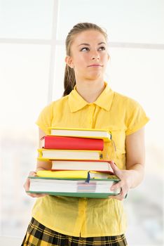 Thinking beautiful teenage girl standing with Colorful books