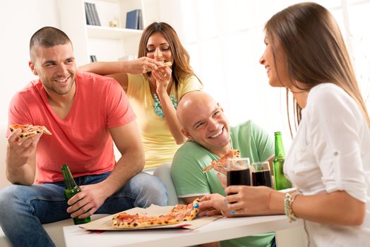 Friends enjoying eating pizza and drink a beer together at home party.