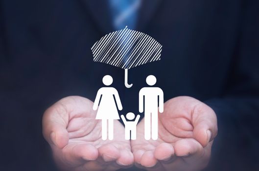 Business man holding a family icon protected by an umbrella 
