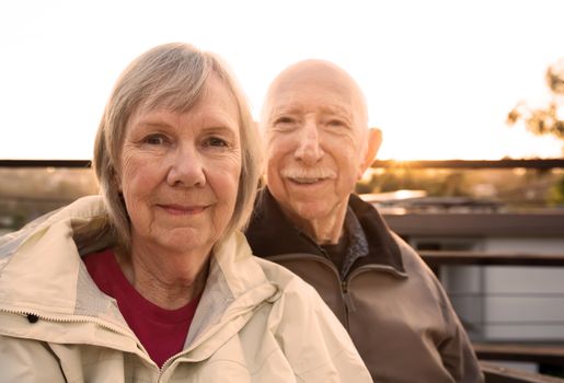 Grinning Caucasian senior couple in jackets sitting outdoors
