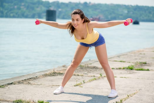 Beautiful girl doing exercise with dumbbell by the river. 