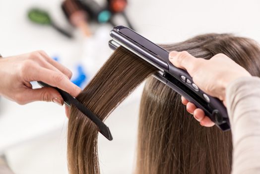 Close-up of a hairdresser straightening long brown hair with hair irons.