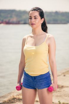 Beautiful girl doing exercise with dumbbell by the river. 