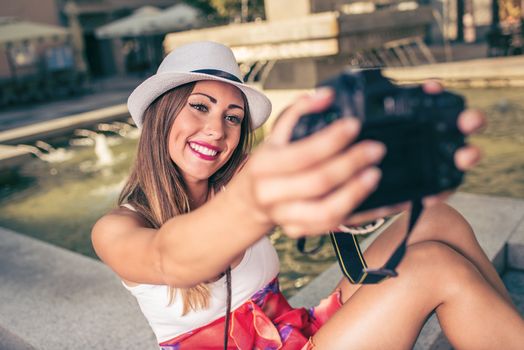Beautiful young woman on vacation taking selfie in the city square next to the fountain.