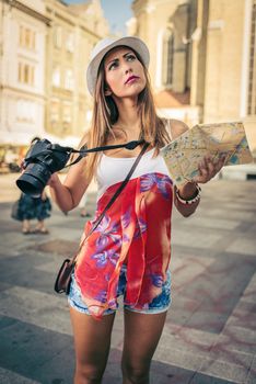Beautiful young girl tourist holding map and photographing with digital camera.