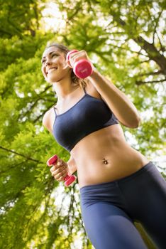 Beautiful girl running with dumbbell in the park. 