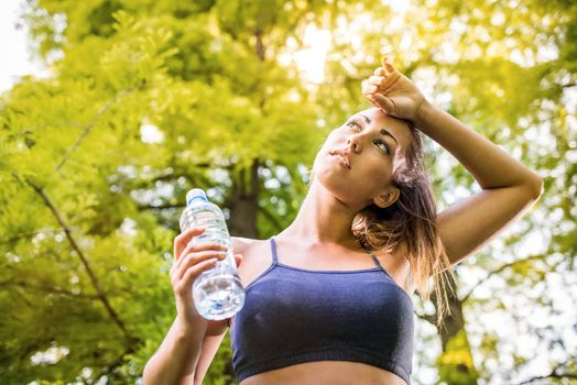 Beautiful young woman holding water bottle after training in the park. 