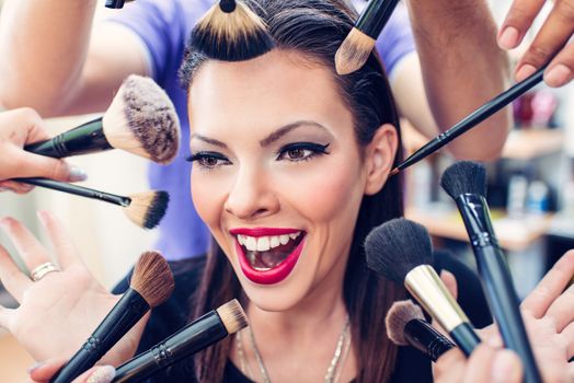 Portrait of a pretty pin-up girl getting make-up applied by a makeup with many  hands. Close up.
