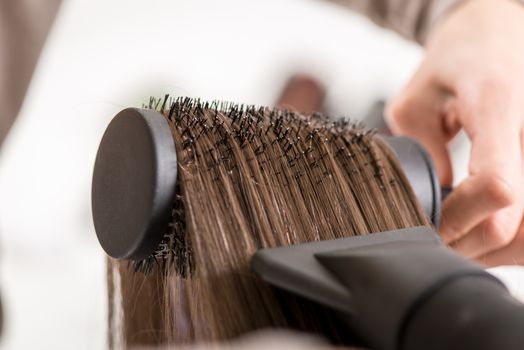 Close-up of a drying brown hair with hair dryer and round brush. 
