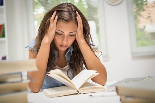 Portrait of tired beautiful teenage girl holding her head and learning.