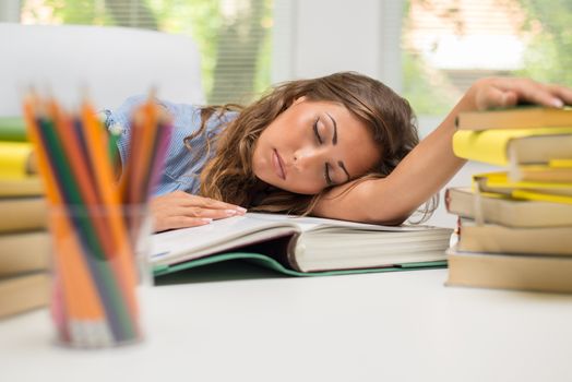 Portrait of beautiful tired teenage girl sleeping on the books in the library.