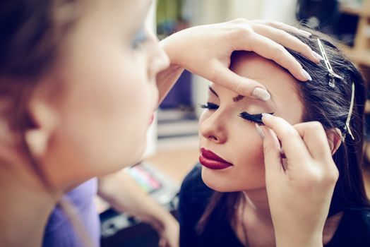 Make-up artist applying the false eyelashes to model. Close up. 